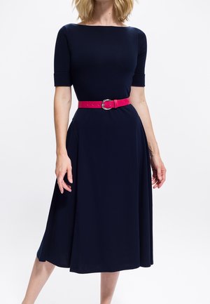 Marineblauwe jurk tot op de knie met een nauwsluitend lijfje, korte mouwen en een uitlopende rok, geaccentueerd door een felroze riem met een zilveren gesp.
