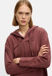 Maroon hooded sweatshirt with a relaxed fit, featuring a kangaroo pocket, textured drawstrings, and embroidered detail on the sleeve.