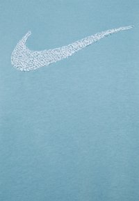 T-shirt di cotone azzurro chiaro con un logo Nike swoosh bianco testurizzato. Il tessuto è morbido con una leggera elasticità, progettato per un abbigliamento informale.