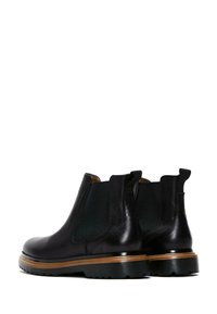 Botas Chelsea de cuero negro con paneles laterales elásticos, suela de goma, acabado texturizado y detalles en marrón contrastante en el borde de la suela.