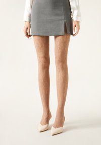 Lace-mønstrede, gennemsigtige nude strømpebukser med et delikat blomstermotiv, parret med et gråt miniskirt og hvide spidse hæle.