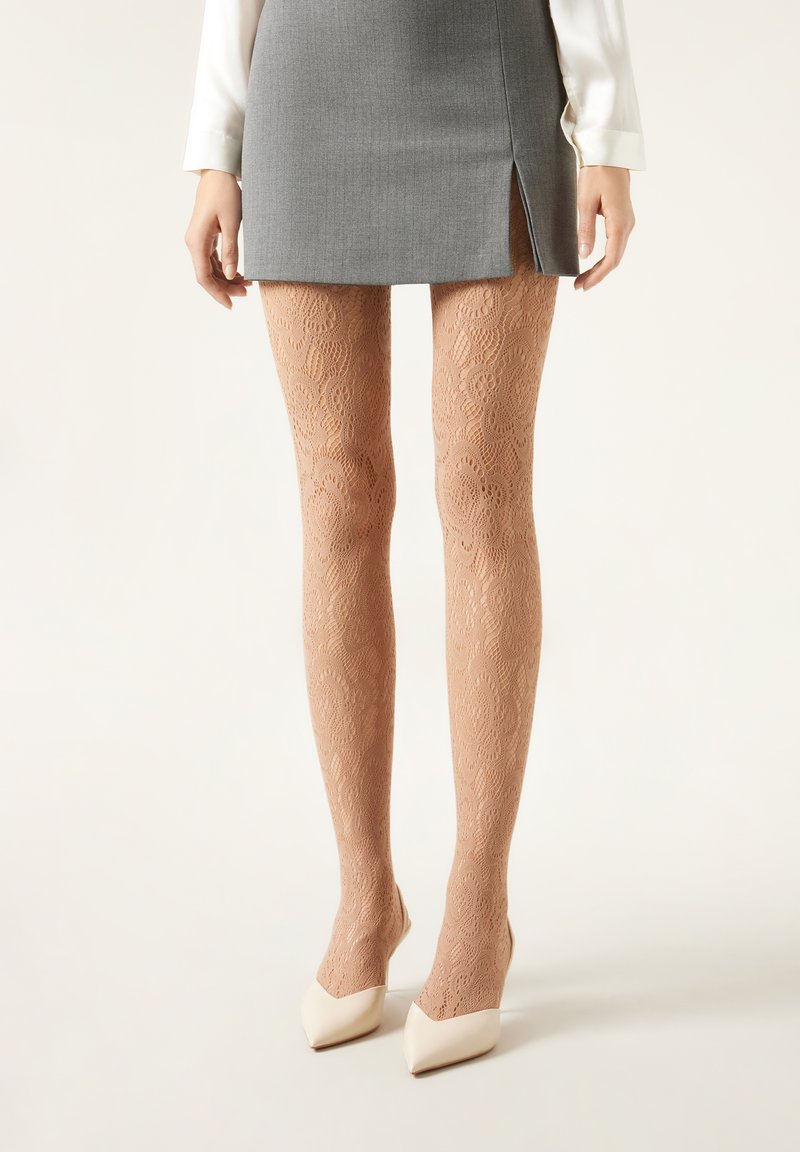 Lace-mønstrede, gennemsigtige nude strømpebukser med et delikat blomstermotiv, parret med et gråt miniskirt og hvide spidse hæle.