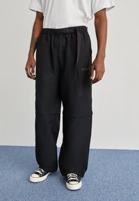 Černé oversized kalhoty s odpovídajícím páskem, vybavené šňůrkou na stažení, ohrnovaným lemem a jemným logem na boku.