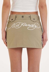 Khaki denim mini sukně s vyšitým logem "Ed Hardy" v bílé barvě, která má dva zapínání na patentky a barevný vyšitý akcent.