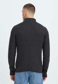 Maglione a collo alto di colore grigio scuro, con un motivo testurizzato e maniche lunghe. Vestibilità casual, indossato con jeans di denim blu.