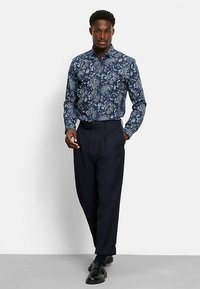 Marineblaues Langarmhemd mit Paisley-Muster, kombiniert mit dunklen Hosen. Das Hemd verfügt über einen Knopfleistenkragen und eine lockere Passform.