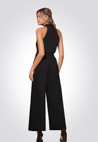 Černý bezramínkový overal s upnutým živůtkem a širokými nohavicemi, vybavený vysokým výstřihem a hladkým, texturovaným materiálem.