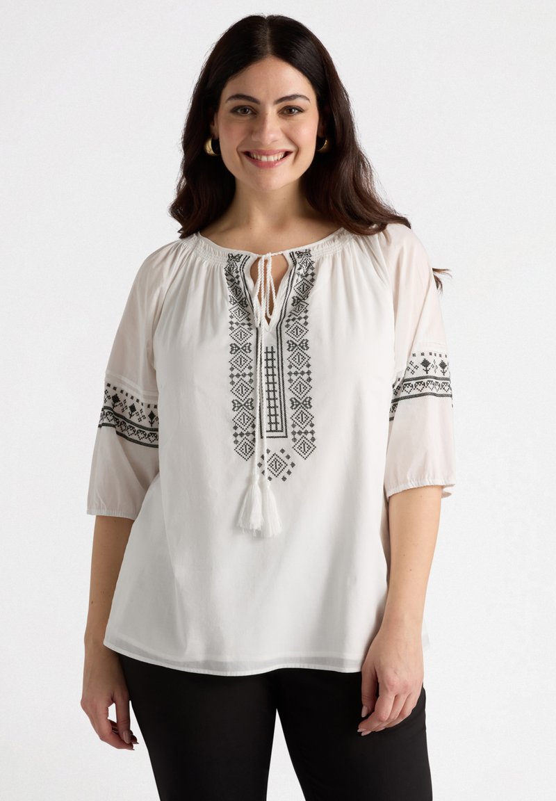 White blouse with black embroidered geometric patterns, keyhole neckline, and 3/4 sleeves, finished with a tassel accent.
