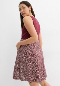 Robe bordeaux avec un haut ajusté et une jupe évasée, ornée d'un motif de léopard blanc. Tissu lisse, sans manches, longueur en dessous du genou.