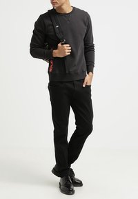 Svart sweatshirt med rund halsringning och ribbade muddars, ihop med svarta byxor. Svarta skor och en axelremsväska med röd text "REPLAY".