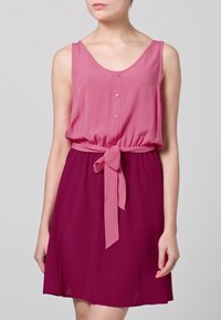 Hihaton, kahdesta väristä koostuva mekko, jossa on vaaleanpunainen yläosa ja tummanpunainen hameosa. Mekossa on nappikiinnitys edessä ja kankainen vyö vyötäröllä. Pinta on sileä.