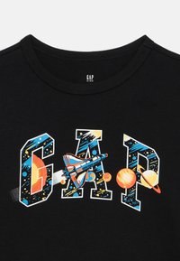 Čierne bavlnené tričko s farebnou vesmírnou tematikou, na ktorej sú nápis "GAP", vesmírna loď a nebeské telesá ako planéty a hviezdy.