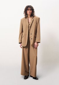 Brauner oversized Blazer und passende weit geschnittene Hose aus einem strukturierten Stoff, mit großen Knöpfen und einer lässigen Passform.