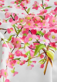 Textil cu un model floral vibrant de flori roz, frunze verzi și ramuri maro pe un fundal din țesătură albă.