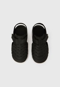 Juodi sandalai iš minkšto guminio su tekstūruotu bangelių raštu, su reguliuojama juostele ir išpjovomis ventiliacijai.