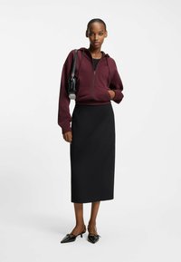 Felpa bordeaux con zip, gonna midi aderente nera e scarpe nere con punta affilata. Tessuto liscio con design minimalista e piccolo dettaglio in metallo.