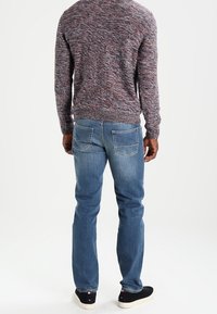 Pull en tricot gris texturé avec un col rond, associé à un jean denim bleu clair avec deux poches arrière et des baskets noires.