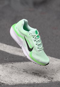 Nike løbesko i lys grøn mesh med sorte accenter, polstret sål og reflekterende detaljer, der viser et slankt, aerodynamisk design.