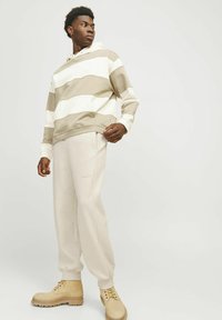 Stribet hættebluse i beige og hvid, parret med lyse beige sweatpants og tan støvler. Lavet af bomuldsstof, afslappet pasform og ribbede manchetter.