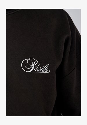 Juodas džemperis su lygiu paviršiumi, kairėje krūtinės pusėje baltas kursyvas logotipas. Paprastas, minimalistinis dizainas.