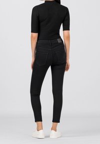 Jeans skinnies negros de denim, con una alta cintura, bolsillos traseros y una parte superior ajustada de textura acanalada. Combinados con zapatillas blancas.