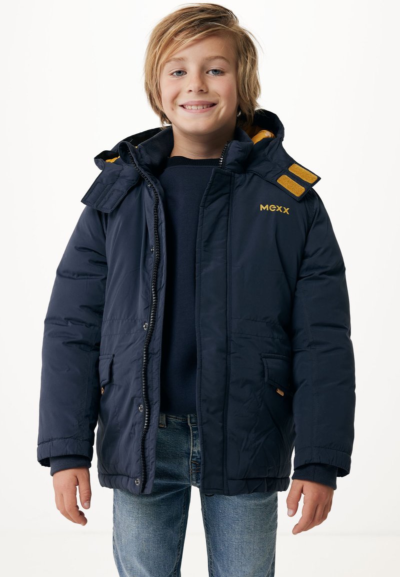 Marinblå pufferjacka med huva, med ett gult foder och orangea detaljer på axlarna. Framzip och tryckknappar för stängning.