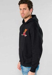 Zwarte hoodie gemaakt van katoen, met een voorzak in kangoeroestijl en een geborduurd graphic van een beer die basketbal speelt. Gelaagd stof.