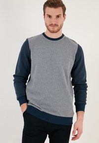 Maglione grigio con maniche blu navy, caratterizzato da un motivo a spina di pesce testurizzato sul davanti e polsini e orlo a costine.