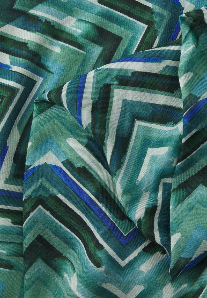 Tissu à motifs verts et bleus présentant des designs en zigzag et en chevrons avec des nuances variées. La texture semble douce et lisse.