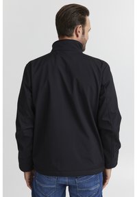 Black softshell jacket featuring a high collar and long sleeves, with a smooth texture and minimal stitching details. Visible blue jeans.