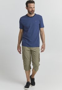 T-shirt à col rond bleu marine à manches courtes associé à un short cargo beige clair avec des poches. Chaussures : baskets noires.