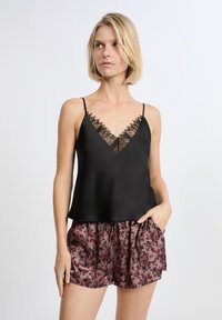 Camisola nera in satin con pizzo sul colletto, abbinata a pantaloni corti rosa a fantasia floreale con tasche laterali.