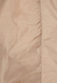Helle beige Stoff mit einer glatten, leicht strukturierten Oberfläche. Verfügt über eine Naht auf einer Seite mit dezenten Stichen.