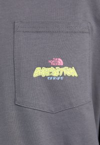 Close-up of a gray fabric pocket with "The North Face Expedition Series" logo in pink, yellow, and blue text on the pocket.