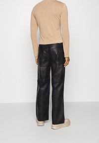 Mörka läderbyxor med en bred bendesign, med bakfickor och synliga sömnadsdetaljer. Tillsammans med en beige långärmad topp.