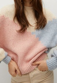 Pletený svetr s volným střihem, který se vyznačuje geometrickým vzorem v pastelově růžové, modré a krémové barvě. Detail žebrovaných manžet a spodního lemu.