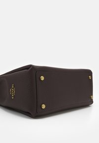 Mørkebrun pebble læder håndtaske bund med guld metalf�ødder og et lille guld Coach New York-logo på siden.