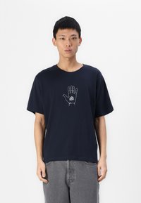 T-shirt in cotone blu navy con maniche corte, caratterizzato da una grafica di una mano bianca e un design a triangolo sul petto. Vestibilità rilassata e scollatura a girocollo.