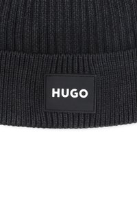 Beanie côtelé noir avec un patch rectangulaire noir portant le logo blanc "HUGO" à l'avant. Texture douce avec un design ajusté.