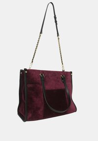 Borsa a tote in suede bordeaux con dettagli in pelle nera, doppi manici e tracolla rimovibile in catena. Presenta una forma strutturata e una texture liscia.