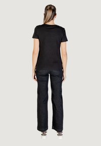 T-shirt nera a maniche corte abbinata a jeans larghi in denim scuro. L'outfit presenta una vestibilità comoda e un design semplice, con dettagli di cucitura delicati.