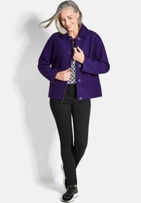 Giacca in misto lana viola con colletto, due tasche frontali e chiusura a bottoni, abbinata a pantaloni neri e sneakers nere.