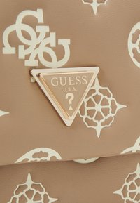 Sac à main beige avec des motifs en relief, doté d'une plaque de logo triangulaire en ton or. Surface texturée avec une finition lisse.