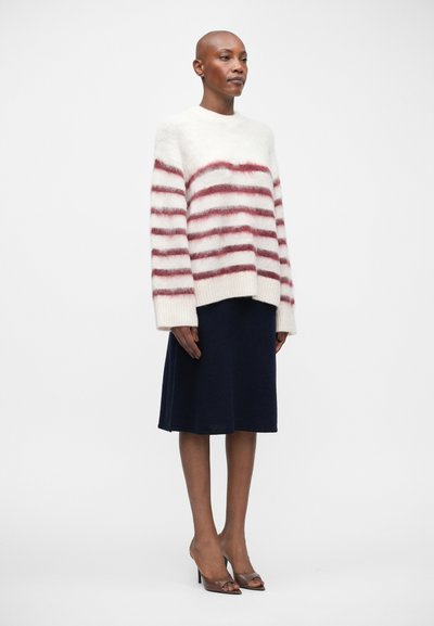 Wit en rood gestreepte wollen trui met een boxy fit, gecombineerd met een donkerblauwe rok tot de knie en bruine open-toed hakken.