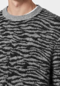 Grå stickad tröja med ett svart vågigt randmönster, rund halsringning och mjuk textur. Lätt och avslappnad design.