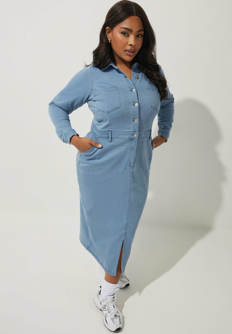 Ljusblå denimklänning med långa ärmar, knäppning fram, två bröstfickor och en sidoklyfta. Bärs med vita sneakers.