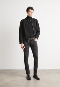 Black denim jacket with a zippered front, paired with a black turtleneck and slim black jeans. Black leather ankle boots complete the outfit.