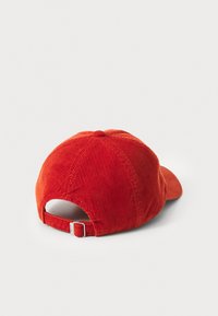 Casquette en velours côtelé rouge avec une visière incurvée, surface texturée et une sangle ajustable à l'arrière. Présente un design classique à six panneaux.