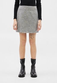 Άτομο που φοράει γκρι μίνι φούστα από τουίντ, μαύρο μακρυμάνικο τοπ, μαύρες δερμάτινες μπότες μέχρι τη μέση της γάμπας και έχει τατουάζ στο δεξί μηρό.