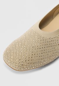 Beežid madalad kingad tekstuuriga pealsega, mis on kaetud sädeleva kivikestega, ümarate varvastega ning paindliku kangast kraega mugavuse tagamiseks.